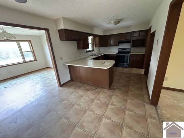 kitchen featuring an inviting chandelier, kitchen peninsula, black range oven, a textured ceiling, and sink