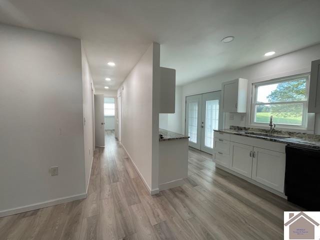 kitchen with sink, light stone countertops, light hardwood / wood-style flooring, white cabinets, and black dishwasher