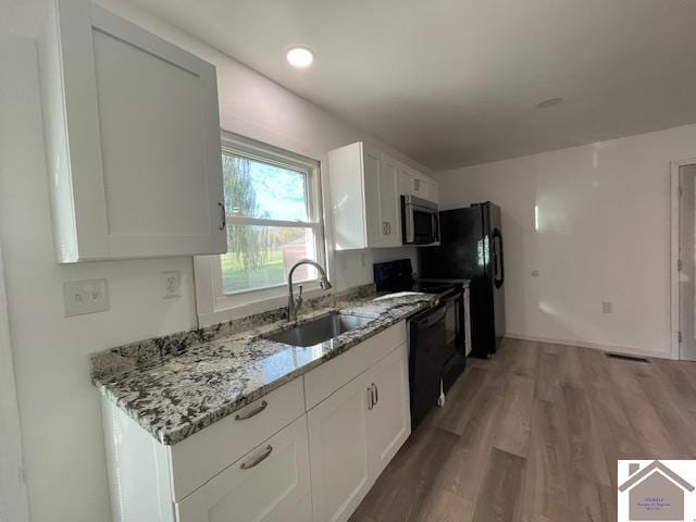 kitchen featuring black appliances, light stone countertops, hardwood / wood-style floors, sink, and white cabinets