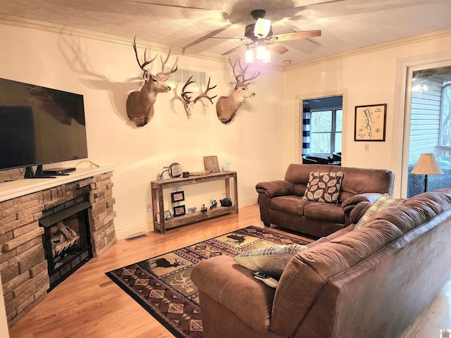 living room featuring ceiling fan, crown molding, hardwood / wood-style floors, a textured ceiling, and a fireplace