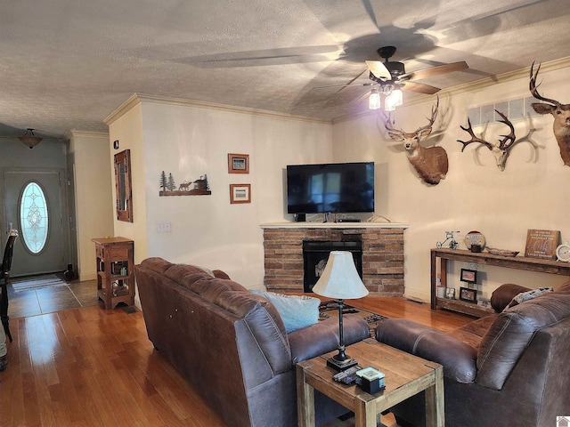 living room featuring a fireplace, crown molding, a textured ceiling, ceiling fan, and wood-type flooring