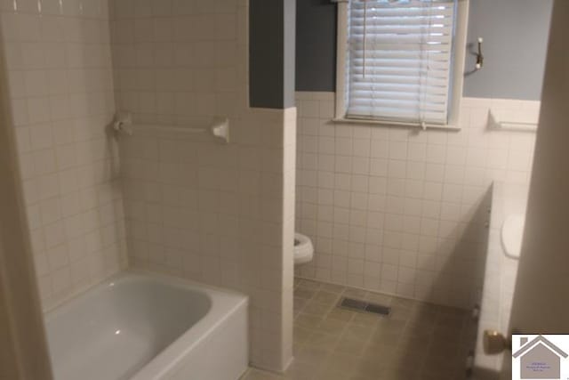 bathroom with toilet, a washtub, tile walls, and tile patterned flooring