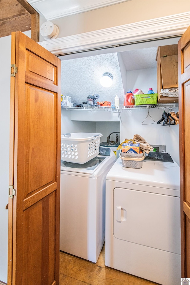 clothes washing area with washer and dryer, a textured ceiling, and light hardwood / wood-style floors