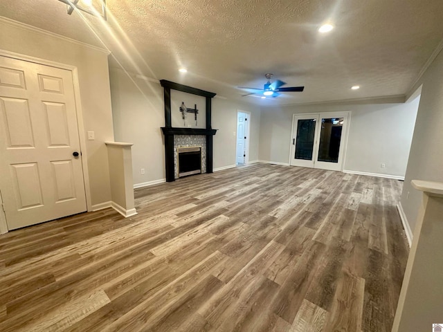 unfurnished living room with a stone fireplace, crown molding, ceiling fan, a textured ceiling, and wood-type flooring