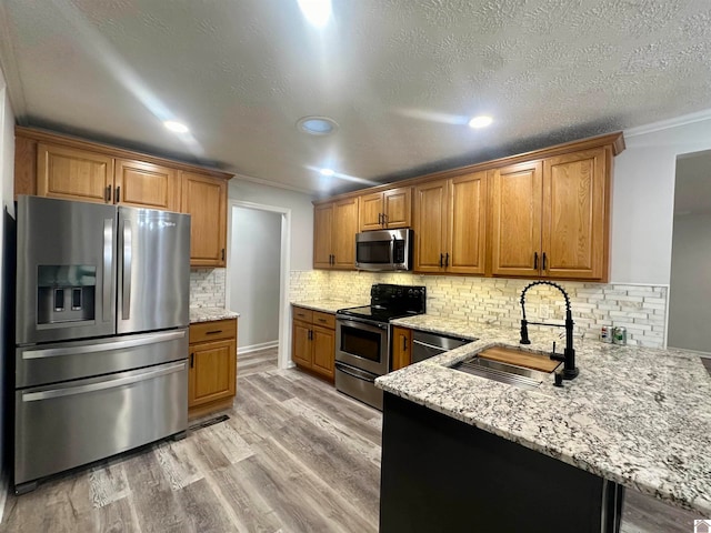 kitchen with appliances with stainless steel finishes, light stone counters, ornamental molding, sink, and light hardwood / wood-style floors