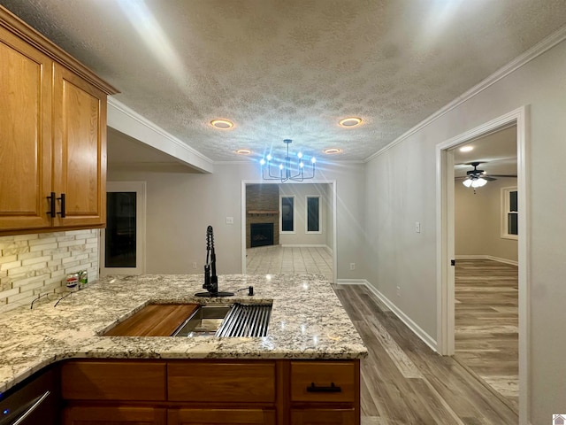 kitchen with ceiling fan, light stone countertops, light wood-type flooring, and crown molding