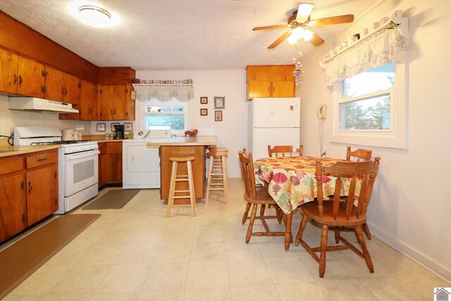 kitchen with a breakfast bar, white appliances, ceiling fan, light tile patterned floors, and washer / clothes dryer