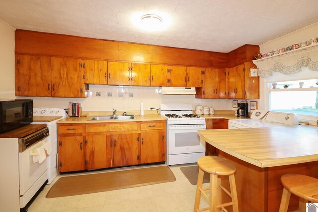 kitchen featuring white gas range, sink, washer / clothes dryer, kitchen peninsula, and a kitchen bar