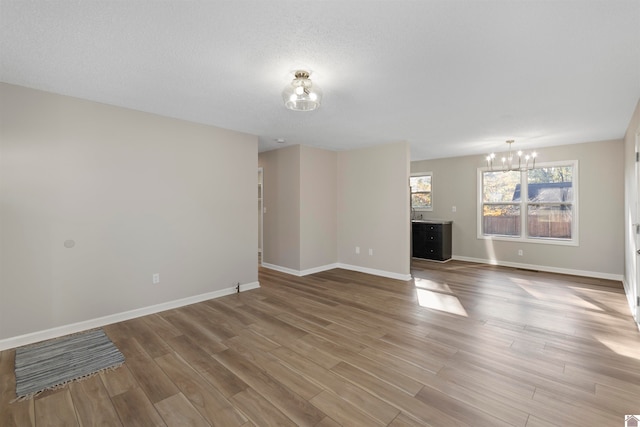 unfurnished living room with wood-type flooring, a textured ceiling, and an inviting chandelier