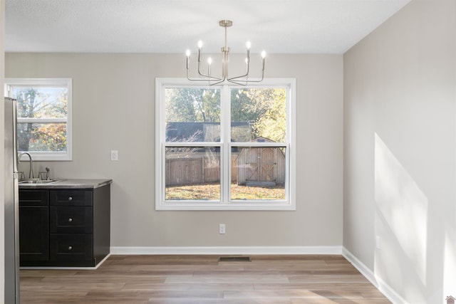 unfurnished dining area with sink, a chandelier, plenty of natural light, and light hardwood / wood-style floors