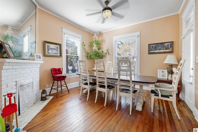 dining room featuring ceiling fan, wood-type flooring, crown molding, and a brick fireplace