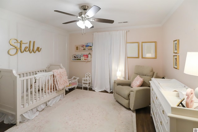 bedroom featuring ceiling fan, dark hardwood / wood-style flooring, a nursery area, and ornamental molding