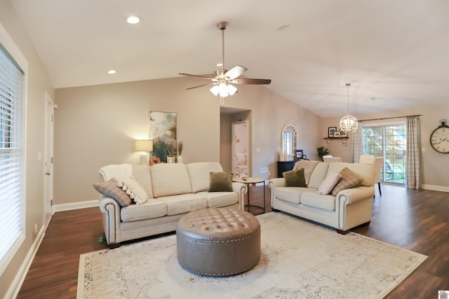 living room featuring ceiling fan with notable chandelier, dark wood-type flooring, and vaulted ceiling