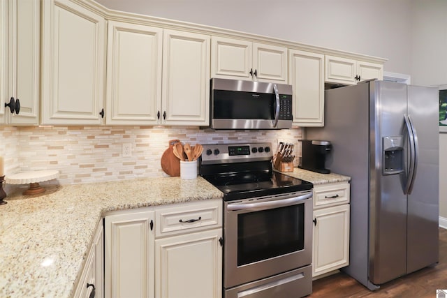 kitchen with light stone counters, dark wood-type flooring, appliances with stainless steel finishes, and cream cabinets