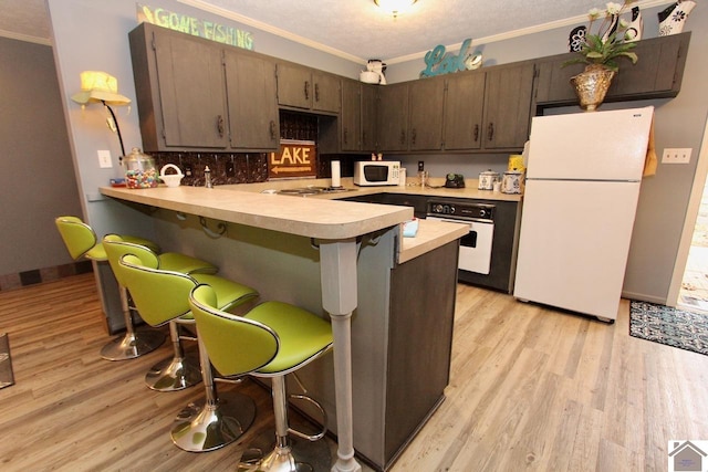 kitchen with kitchen peninsula, dark brown cabinets, white appliances, crown molding, and light hardwood / wood-style flooring