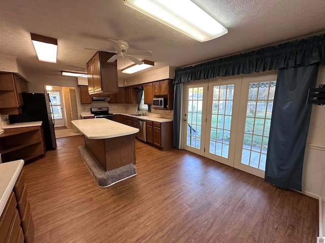 kitchen with hardwood / wood-style flooring, a kitchen island, a textured ceiling, and appliances with stainless steel finishes