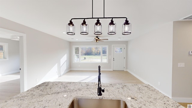 kitchen with ceiling fan, light stone countertops, light wood-type flooring, and sink