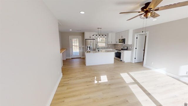 kitchen with light wood-type flooring, stainless steel appliances, a kitchen island, decorative light fixtures, and white cabinetry