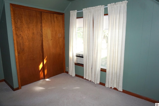 unfurnished bedroom featuring light colored carpet, vaulted ceiling, a closet, and wooden walls