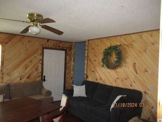 living room with ceiling fan, a textured ceiling, and wooden walls