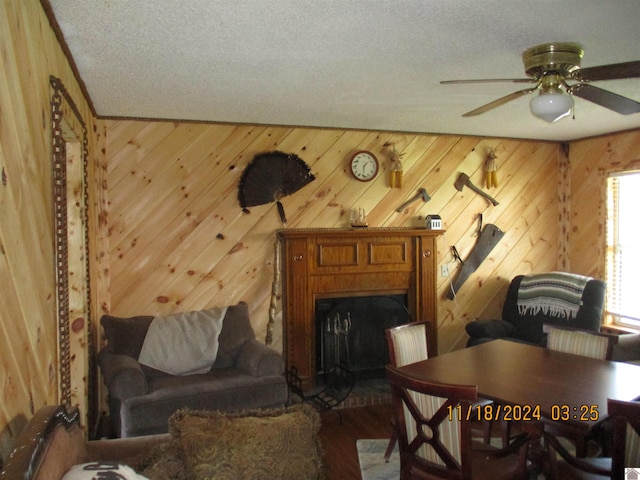 living area featuring hardwood / wood-style floors, ceiling fan, a textured ceiling, and wooden walls