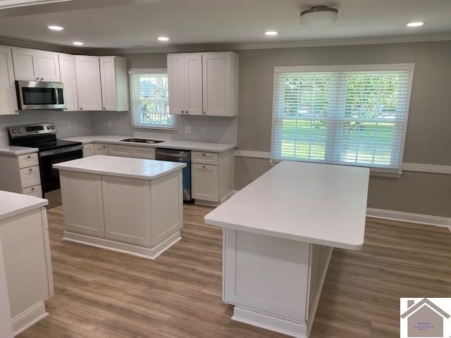 kitchen featuring white cabinetry, appliances with stainless steel finishes, crown molding, a kitchen island, and light wood-type flooring