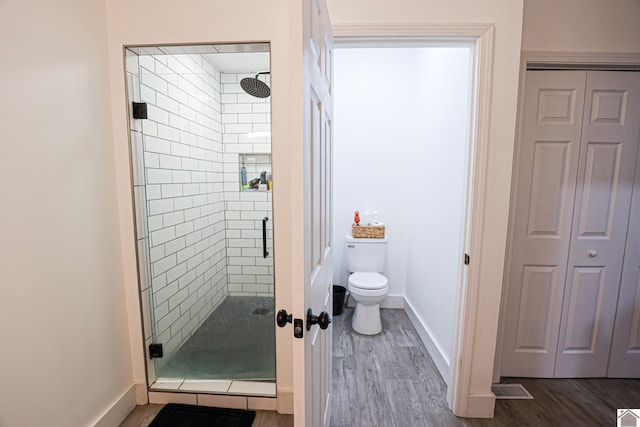 bathroom with wood-type flooring, a shower with shower door, and toilet