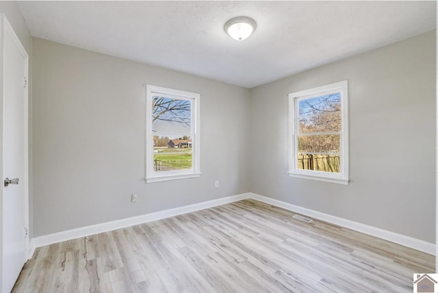 empty room with a textured ceiling, light hardwood / wood-style flooring, and a healthy amount of sunlight