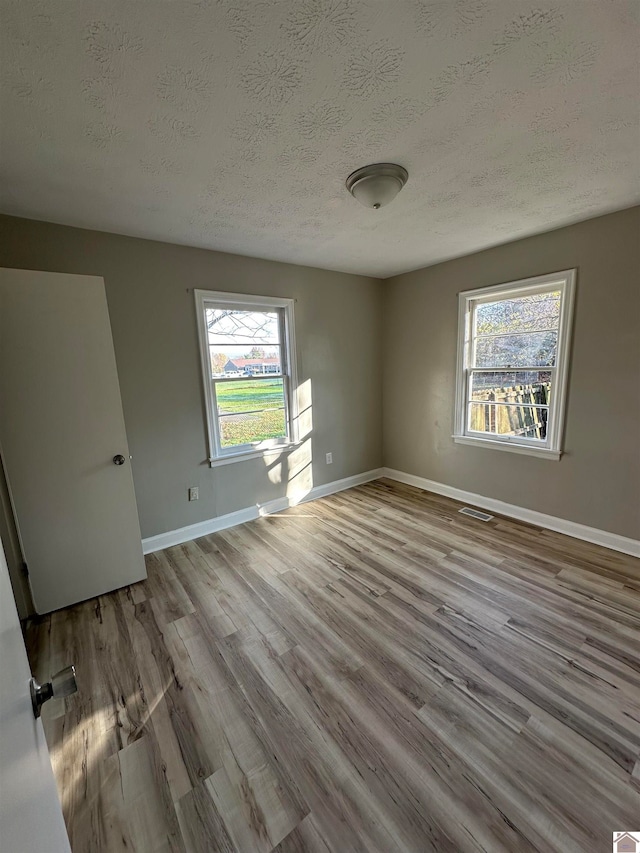 unfurnished room with a textured ceiling and light hardwood / wood-style flooring