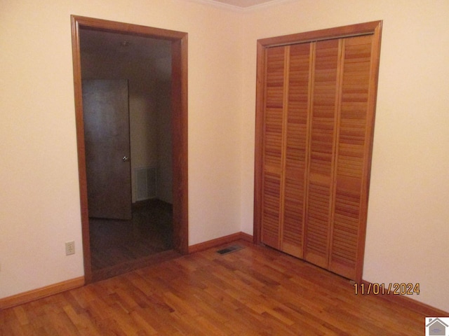 unfurnished bedroom with hardwood / wood-style floors, a closet, and crown molding