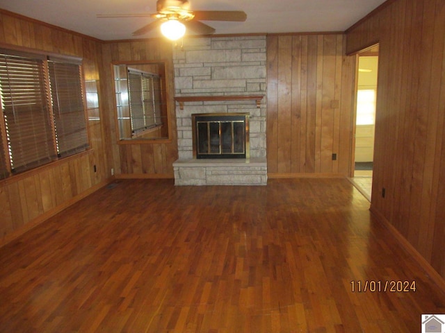 unfurnished living room with ceiling fan, wood walls, dark wood-type flooring, and a fireplace