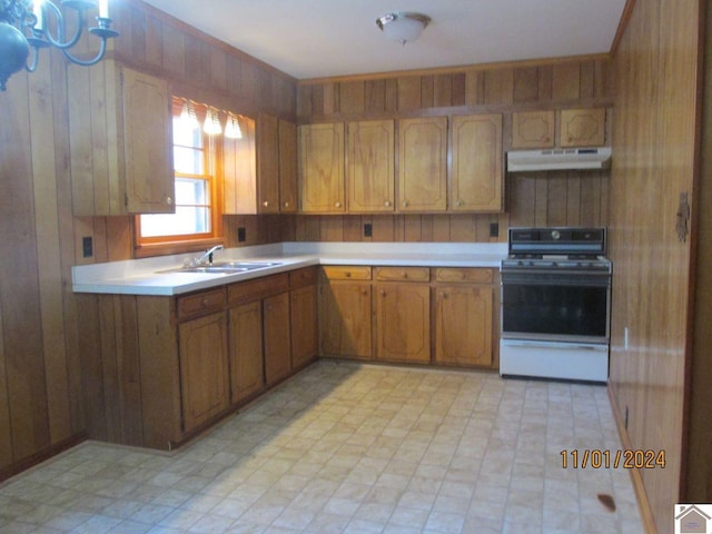 kitchen with white range with gas cooktop, wood walls, and sink