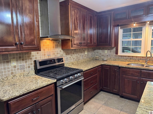 kitchen with light stone countertops, wall chimney range hood, sink, light tile patterned floors, and stainless steel range with gas cooktop