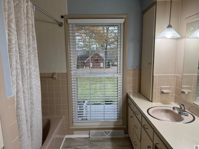 bathroom with shower / bath combo with shower curtain, vanity, a healthy amount of sunlight, and tile walls