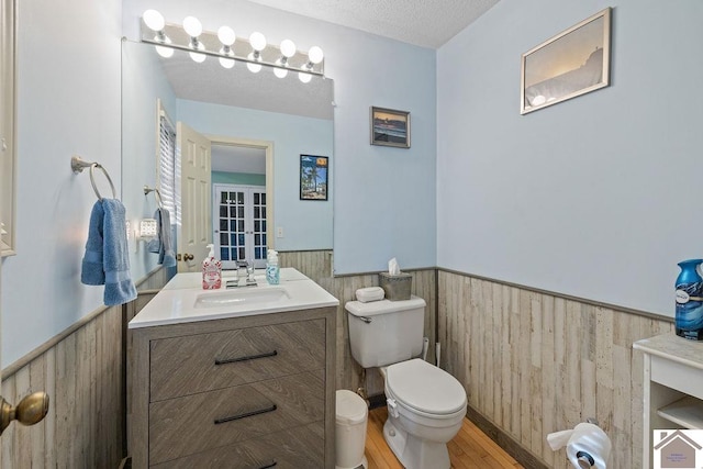 bathroom featuring vanity, wood walls, toilet, a textured ceiling, and wood-type flooring