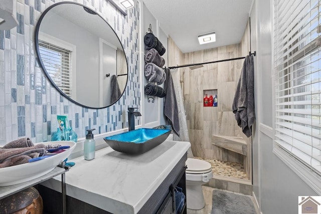 bathroom with toilet, a tile shower, a textured ceiling, and vanity