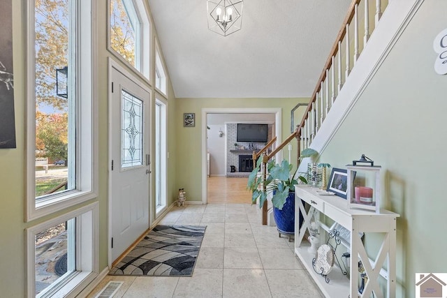 tiled foyer entrance featuring a fireplace, a chandelier, and high vaulted ceiling