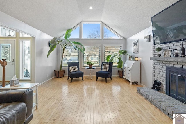 living area with a brick fireplace, light hardwood / wood-style floors, a textured ceiling, and vaulted ceiling