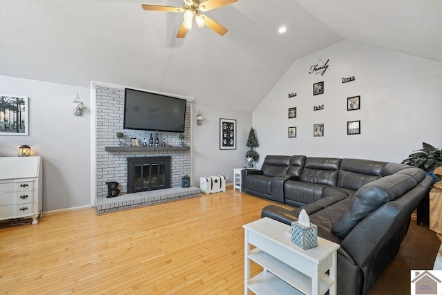 living room featuring a brick fireplace, light hardwood / wood-style floors, vaulted ceiling, and ceiling fan