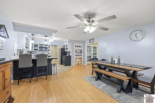 dining area with ceiling fan, light wood-type flooring, and a textured ceiling