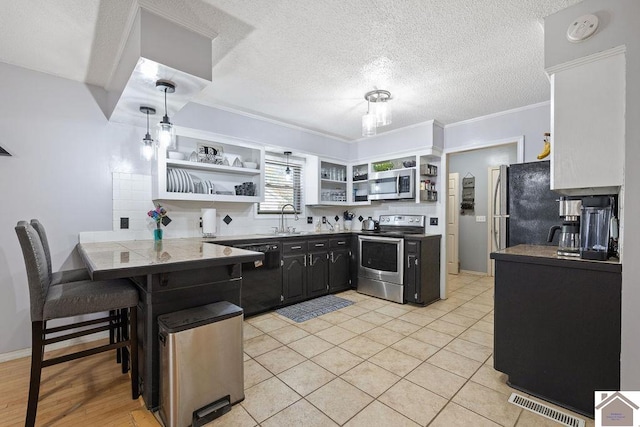 kitchen with sink, ornamental molding, appliances with stainless steel finishes, kitchen peninsula, and a breakfast bar area