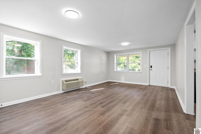 empty room featuring dark hardwood / wood-style floors, a wall unit AC, and a wealth of natural light