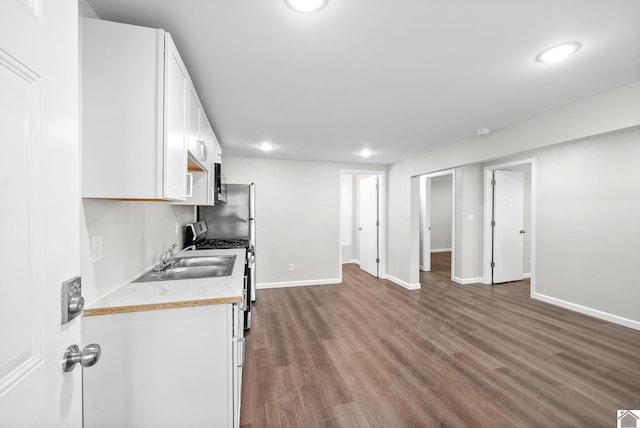 kitchen with wood-type flooring, gas range, white cabinetry, and sink