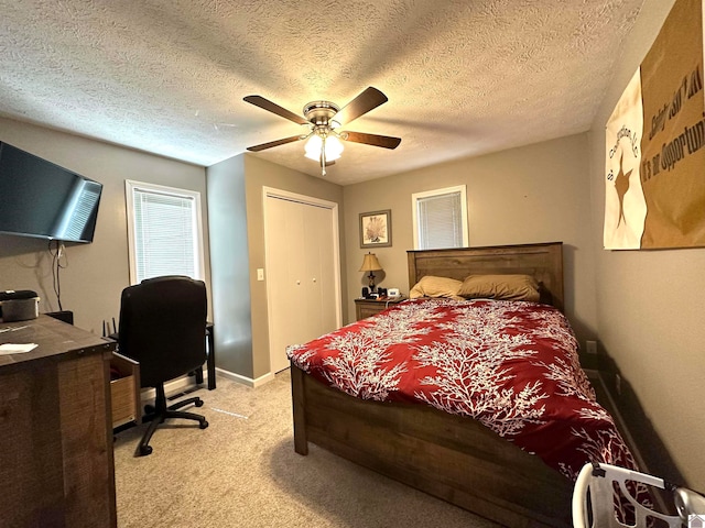 bedroom featuring ceiling fan, a closet, light colored carpet, and a textured ceiling