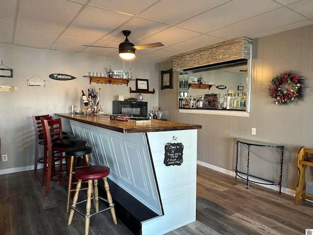 bar featuring ceiling fan, dark wood-type flooring, wood counters, wood walls, and a paneled ceiling