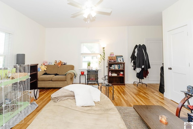 living room with ceiling fan, wood-type flooring, and a wood stove