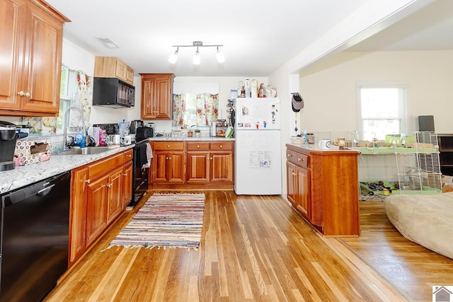 kitchen featuring sink, light hardwood / wood-style floors, light stone counters, and black appliances