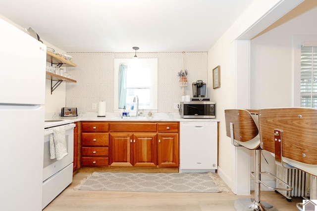 kitchen featuring white appliances, radiator, sink, hanging light fixtures, and light wood-type flooring