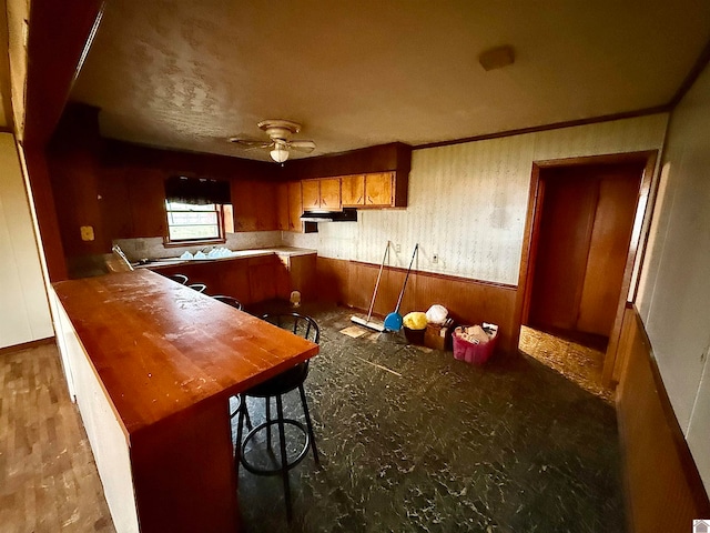 kitchen featuring kitchen peninsula, a breakfast bar, ceiling fan, and wooden walls