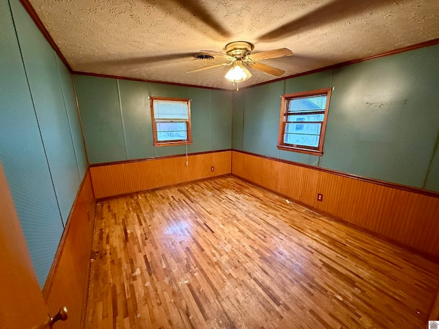 spare room with wood walls, ceiling fan, light hardwood / wood-style floors, and a textured ceiling